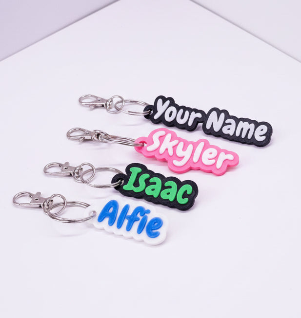 Four keychains with personalized names in different colors on a light purple background