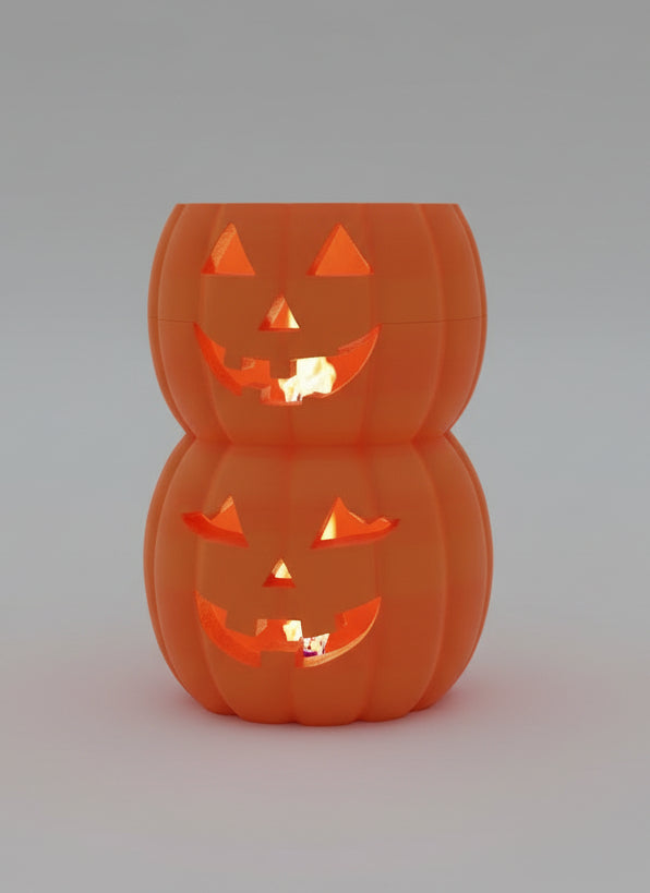 A stacked set of two orange jack-o'-lantern-shaped containers with carved faces, sitting on a dark shelf in front of a window.